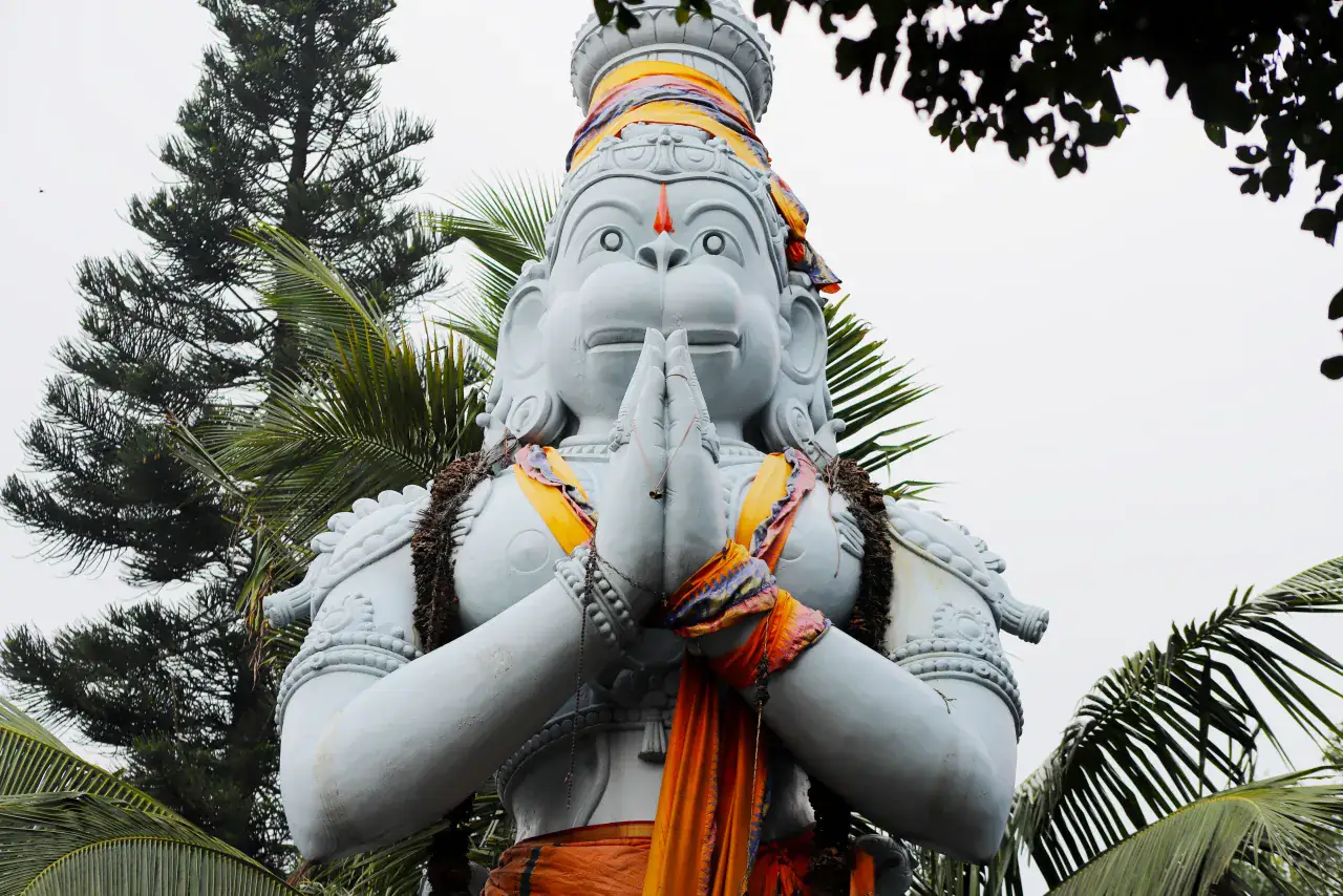 A large white image of Hanuman with folded hands among palm trees