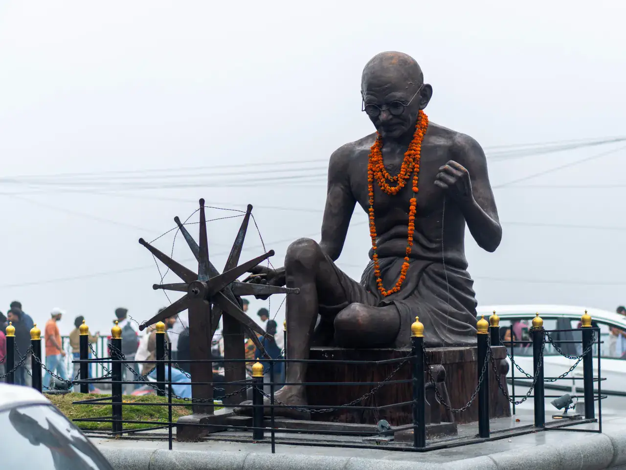 A flower-garlanded statue of Mahatma Gandhi with a spinning wheel