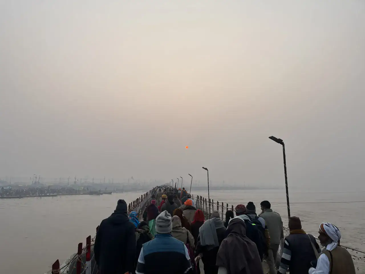 Pilgrims walking along a pontoon approach to the Sangam in morning mist
