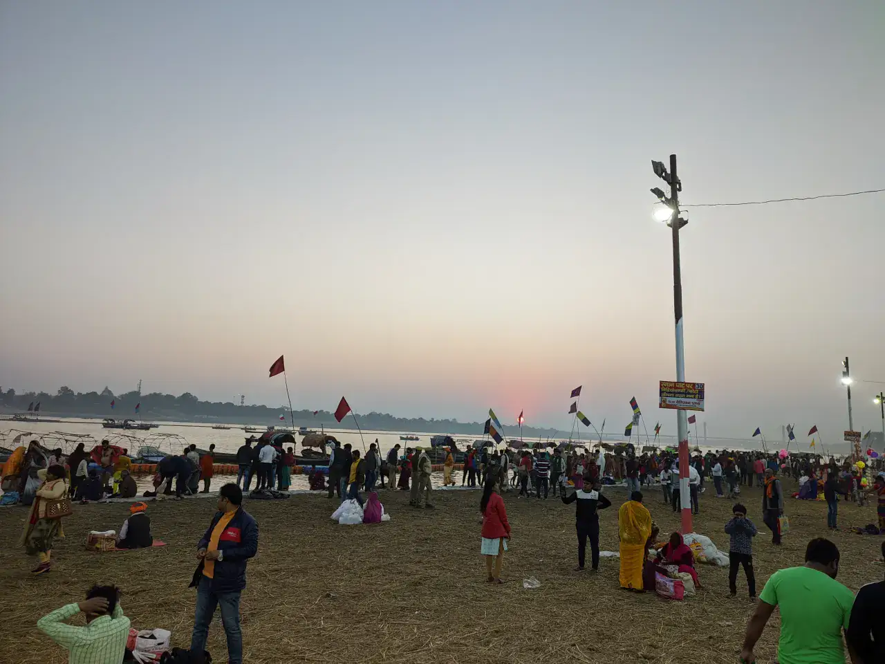 Pilgrims beside boats on the Triveni Sangam riverbank at dusk