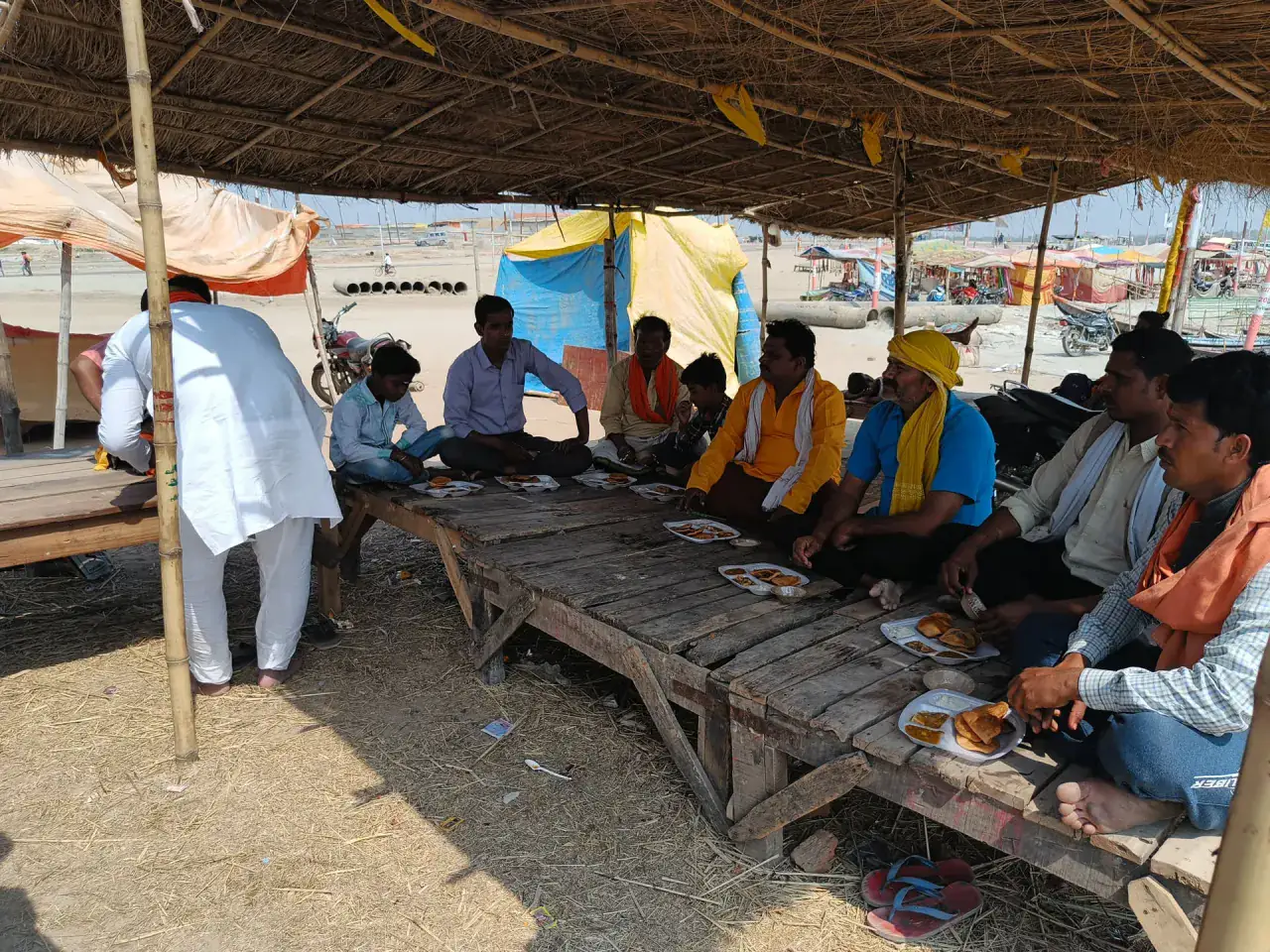 A pilgrimage group sharing a meal beneath a shelter in Prayagraj
