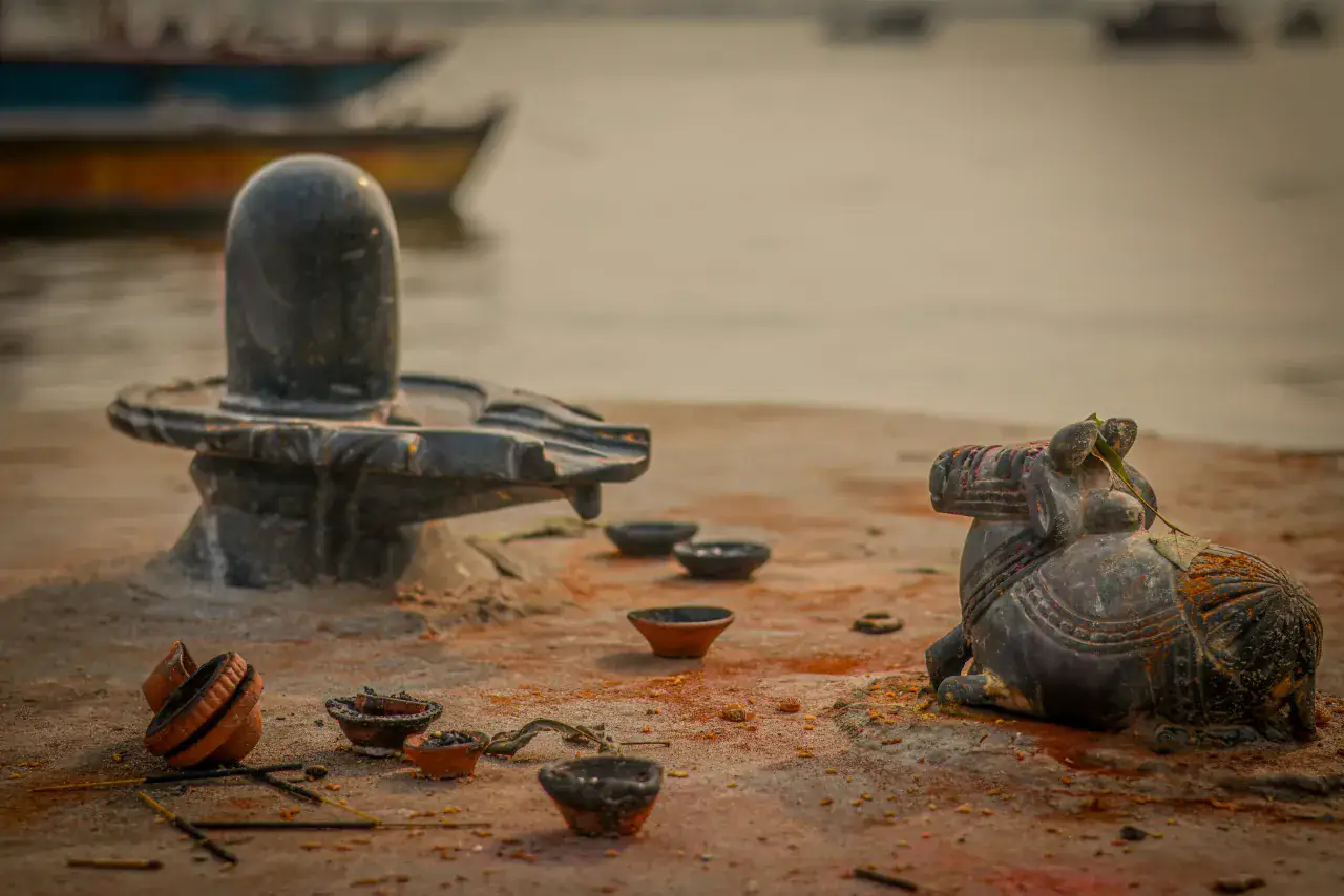 A Shiva linga and Nandi beside a riverbank with small lamps set around them